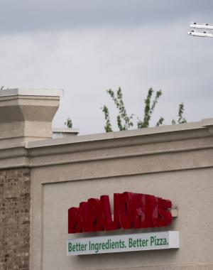 A drone carrying a Papa Johns order flying over a Papa Johns restaurant