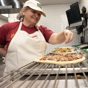 Papa Johns team member applying toppings to pizza