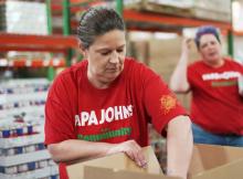 A Papa Johns volunteer packs meals at a food bank