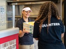 A Papa Johns team members hands surplus pizza orders to a volunteer.